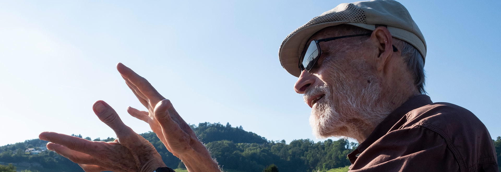 Audiodescrição (AD): foto de um homem que aparece de perfil, do peito para cima. Ele é branco, tem barba branca, usa óculos escuros e um boné. Imagem 1 de 1