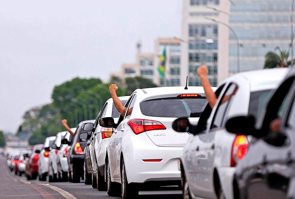 Foto que mostra carros enfileirados em uma avenida.