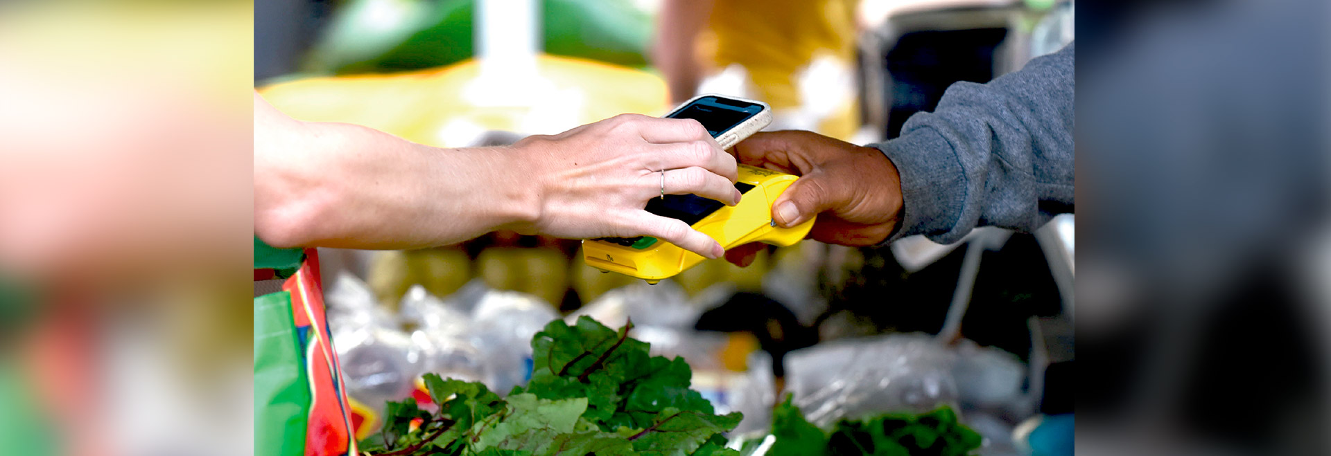 Audiodescrição: foto que mostra cena de uma pessoa pagando uma conta com cartão de crédito em uma feira livre. Imagem 1 de 1