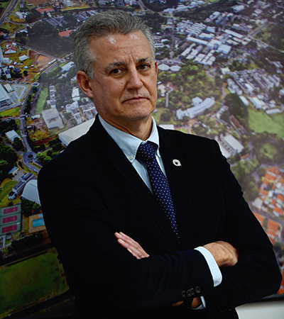 Foto de um homem que aparece da cintura para cima e está com os braços cruzados. Ele é branco, tem o cabelo curto e usa terno escuro e gravata.