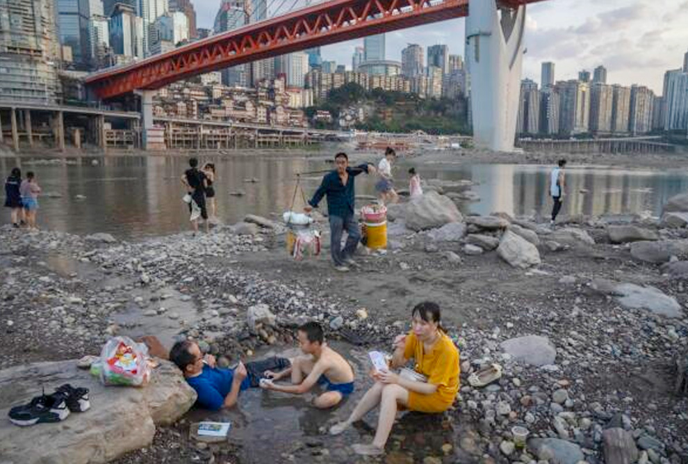 Pessoas sentadas em uma piscina rasa de água no leito do rio Jialing, um afluente do Yangtze, no município de Chongqing, no sudoeste da China, no sábado, 20 de agosto de 2022. A própria paisagem de Chongqing, uma megacidade que também abrange terras agrícolas nos arredores e montanhas íngremes e pitorescas, foi transformada por uma onda de calor excepcionalmente longa e intensa e uma seca que a acompanhou. Fonte: Mark Schiefelbein, Associated Press