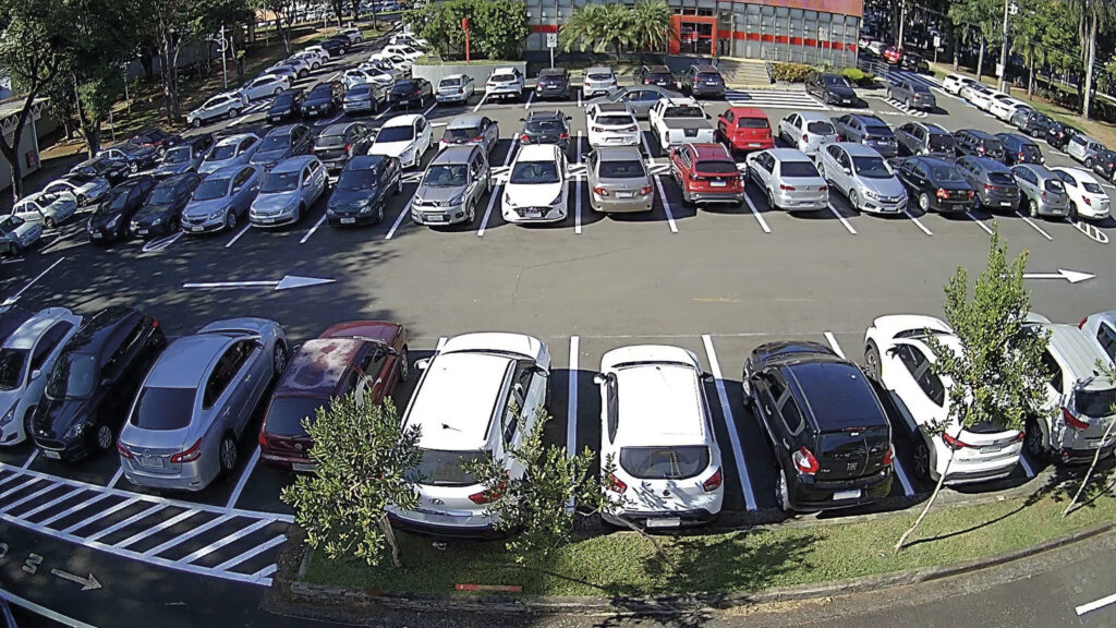 Estacionamento externo, bem organizado, com grande número de veículos estacionados. A imagem foi registrada em um dia claro e ensolarado