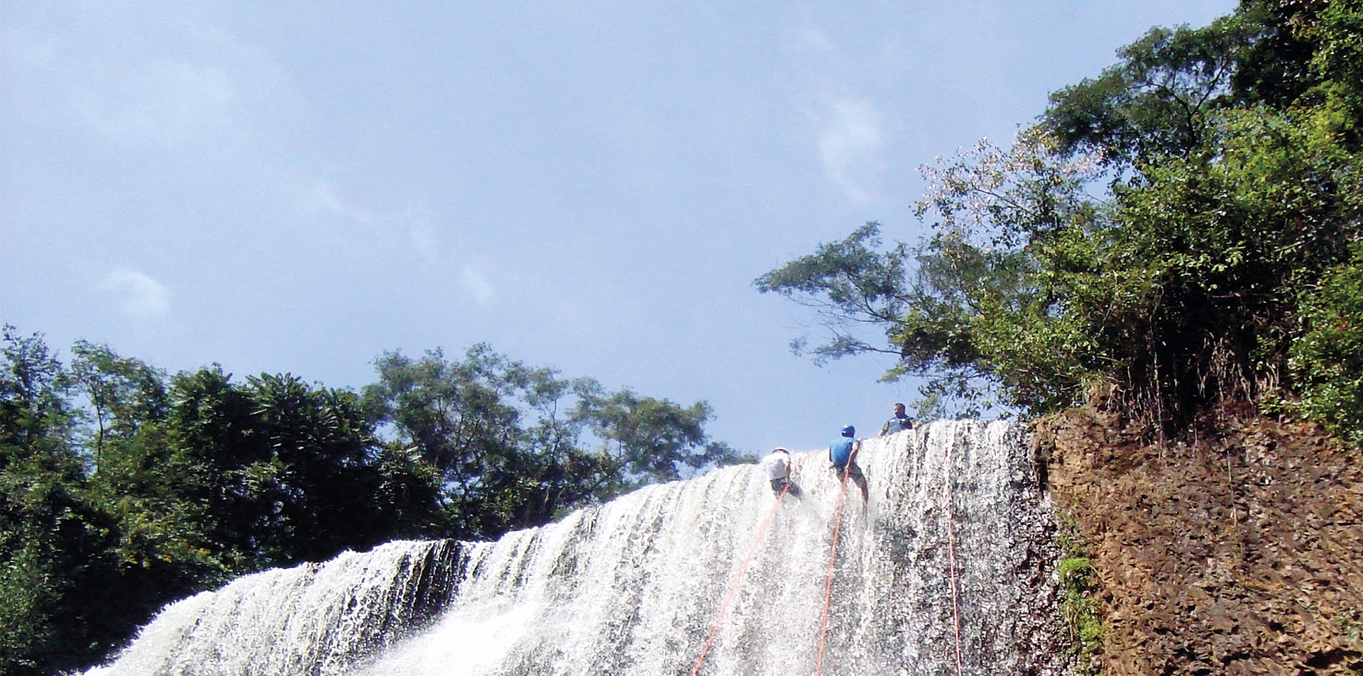 Imagem mostra uma cachoeira na cidade Brotas, com dois praticante de Rapel, pendurados iniciando a descida da cachoeira