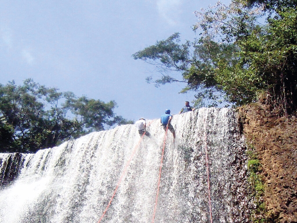 Imagem mostra uma cachoeira na cidade Brotas, com dois praticante de Rapel, pendurados iniciando a descida da cachoeira