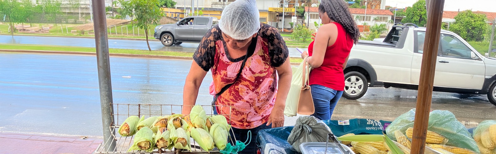 banca de frutas e mulheres próximas, com carro passando na rua ao fundo