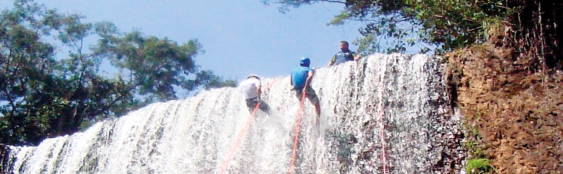 Imagem mostra uma cachoeira na cidade Brotas, com dois praticante de Rapel, pendurados iniciando a descida da cachoeira