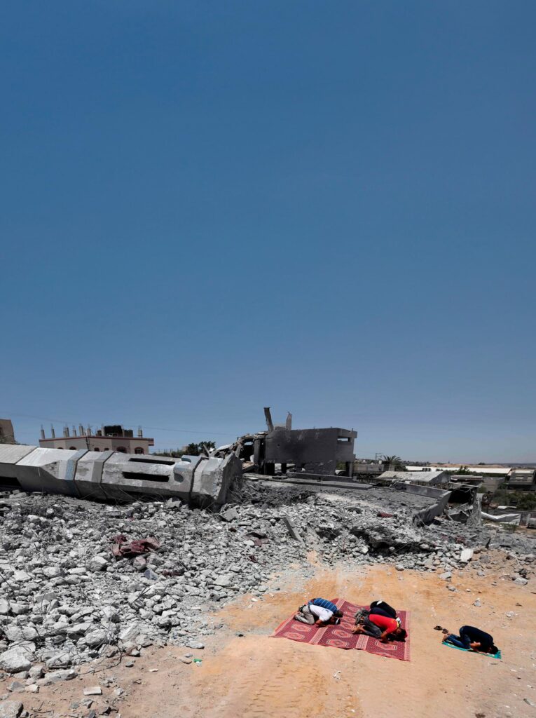 Imagem mostra palestinos durante oração diante de prédio destruído