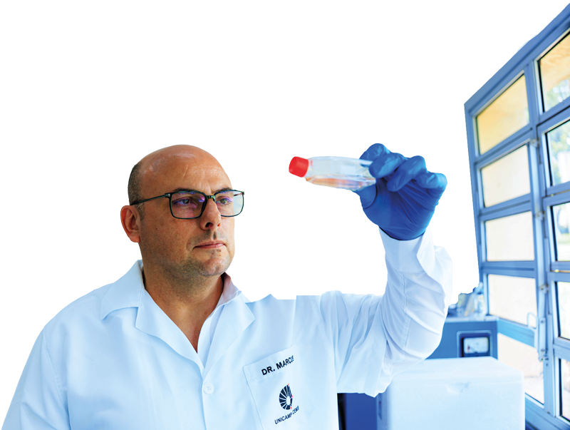A imagem mostra um homem de óculos e jaleco branco, segurando um pequeno frasco de laboratório com tampa vermelha na altura dos olhos. Ele usa uma luva azul na mão que segura o frasco e observa o conteúdo com atenção. Ao fundo, à direita, vê-se uma janela com várias divisórias de vidro e parte de equipamentos laboratoriais, enquanto o restante do fundo é branco e liso.